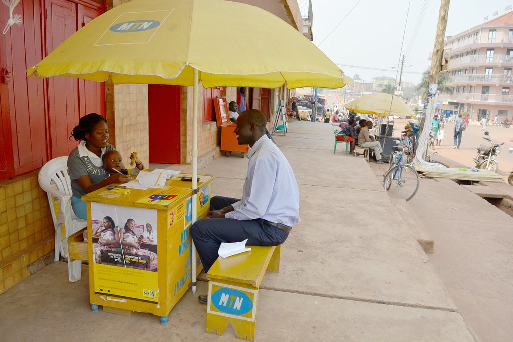 MTN female attendant attending to a black male customer seated on a yellow bench under an MTN umbrella