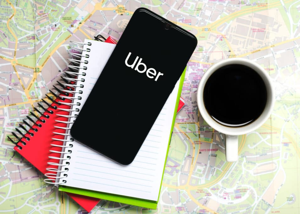 2400 uber application icon on black screen of smartphone with notebooks and cup of coffee