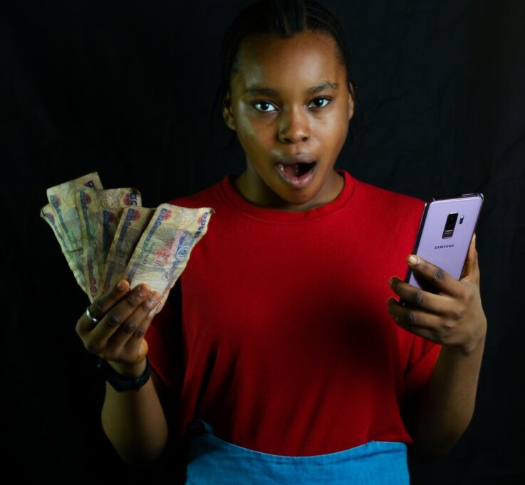 Lady holding smartphone and cash looking shocked