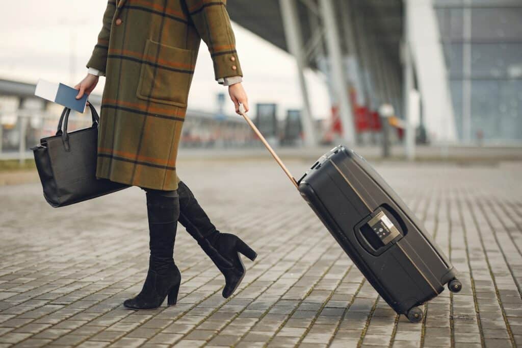 stylish woman with suitcase and bag walking on street near modern airport terminal