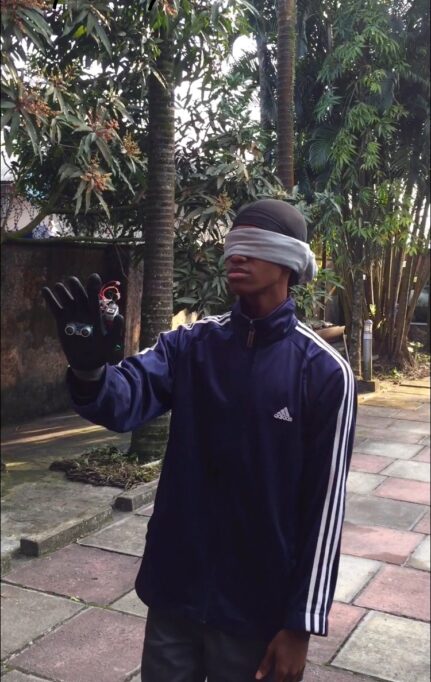 A young man in blindfolds, holding out his hand that has an unusual glove worn on it.