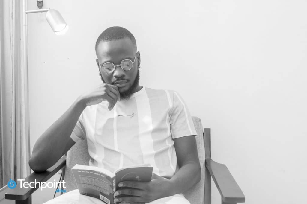 An image of Daniel Orubo. Head of content and content strategy, Piggyvest sitting beside a lamp and reading a book